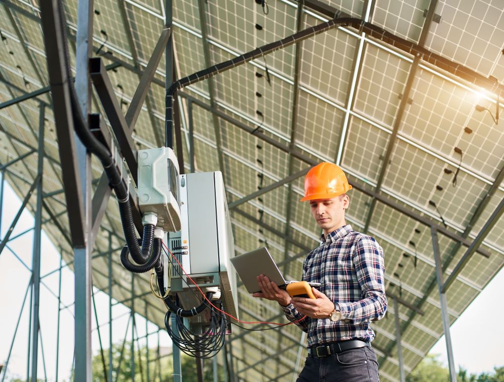 Smiling guy with laptop and sensor in the background of the solar power station